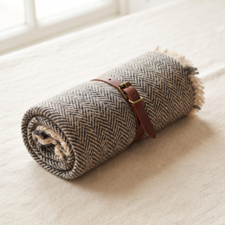 Rolled Wool Travel Blanket in charcoal and oat herringbone wool, buckled into a leather carry strap