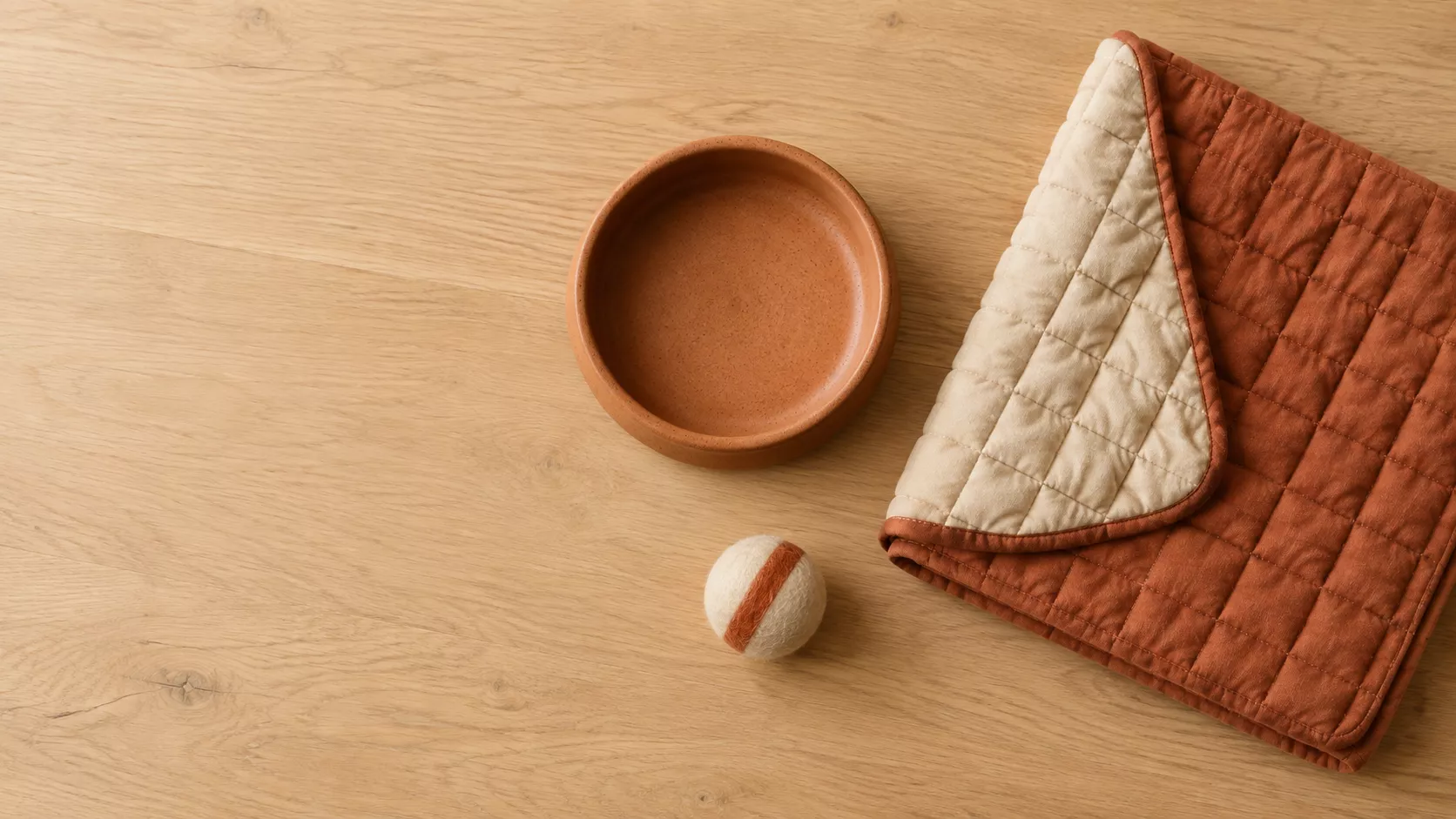 A terracotta stoneware bowl, a quilted cotton mat and a felted wool ball on an oak floor